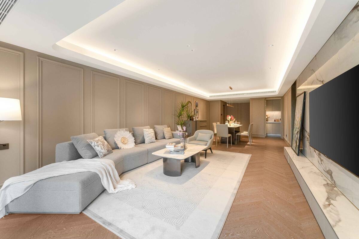 Ein modernes Wohnzimmer mit einem grauen Ecksofa, einem Couchtisch und einem Essbereich im Hintergrund.