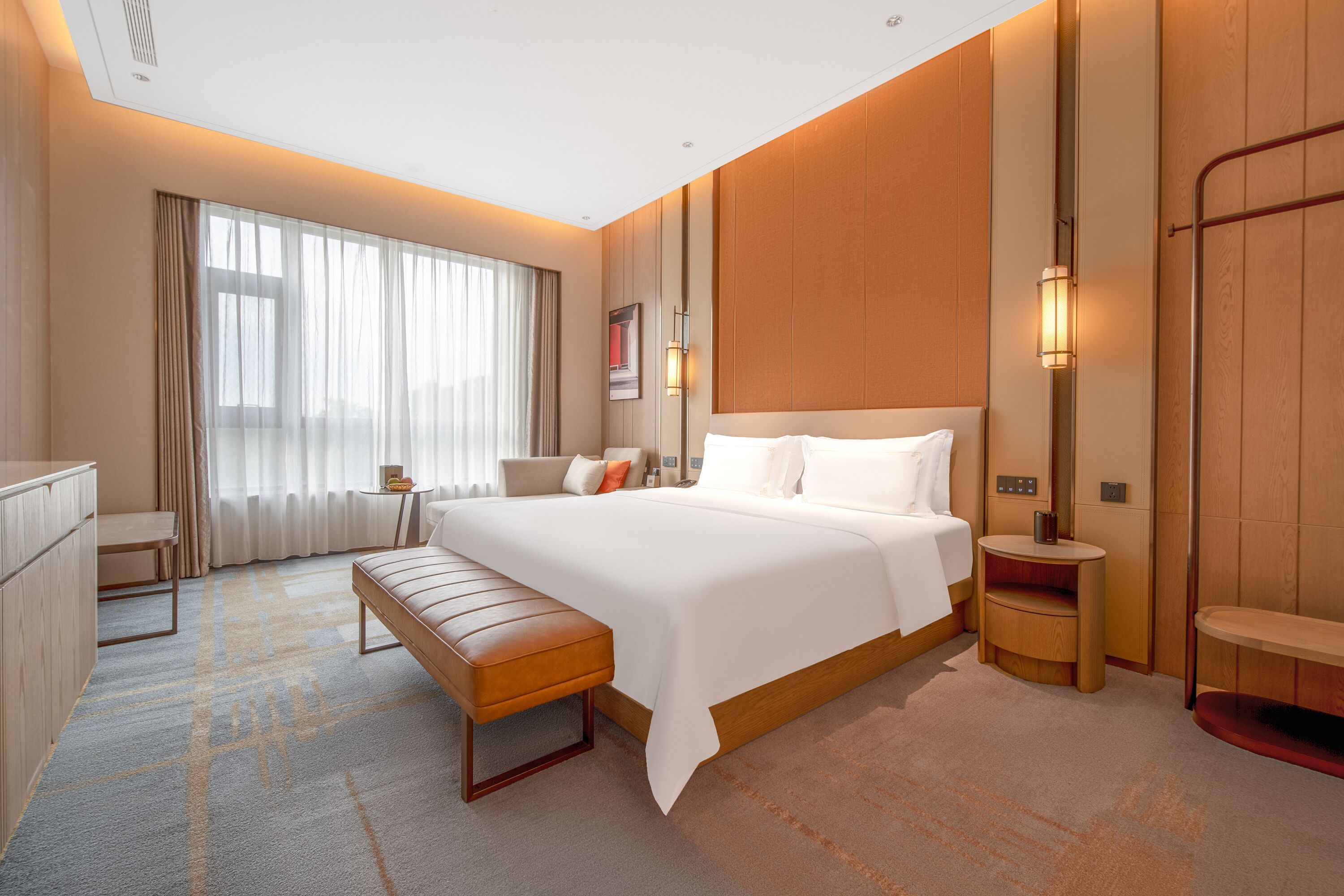Quarto de hotel moderno com uma cama grande, uma escrivaninha, um banco e uma pequena mesa.