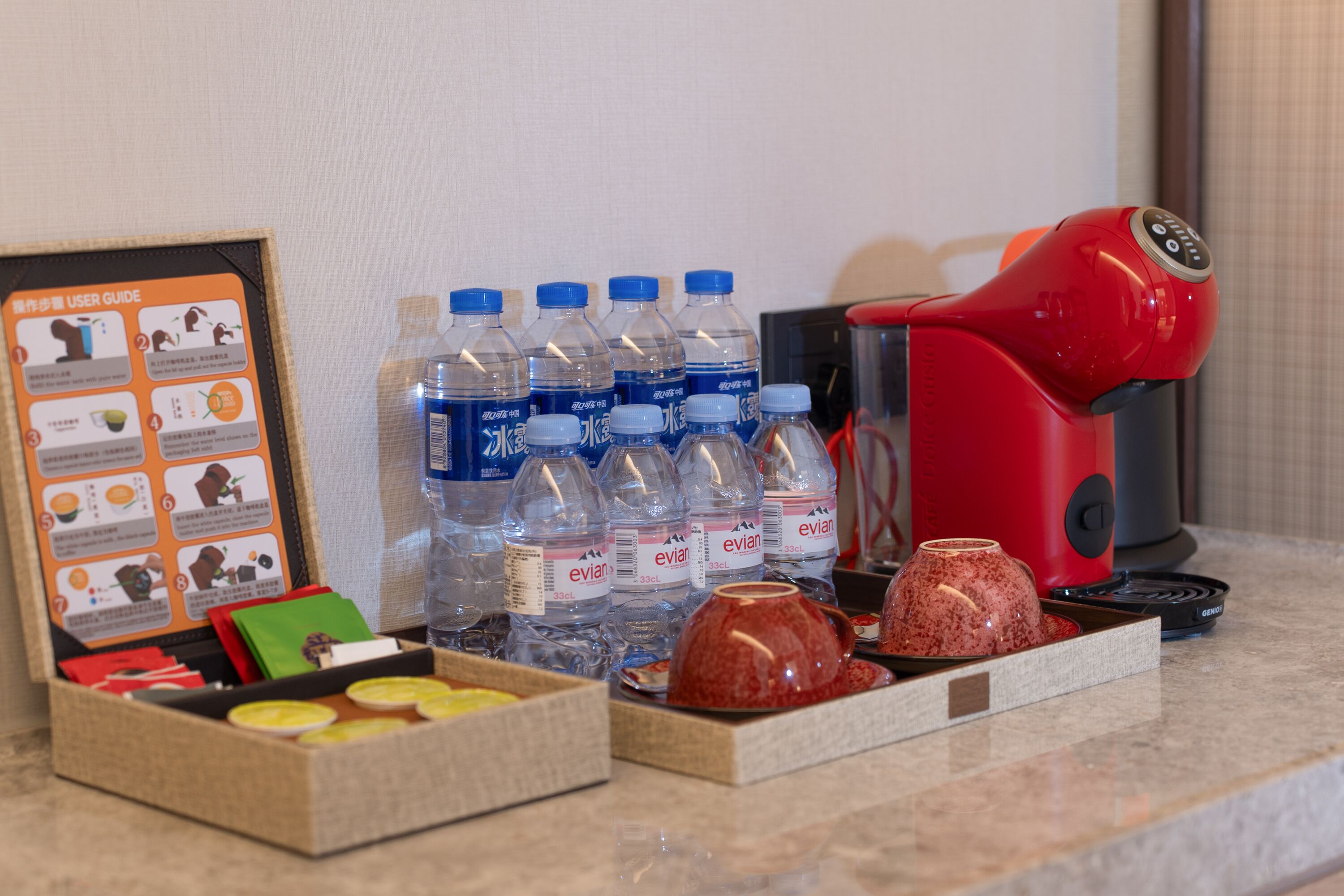 A breakfast setup with Evian water bottles, a red coffee maker, and a user guide on the counter.