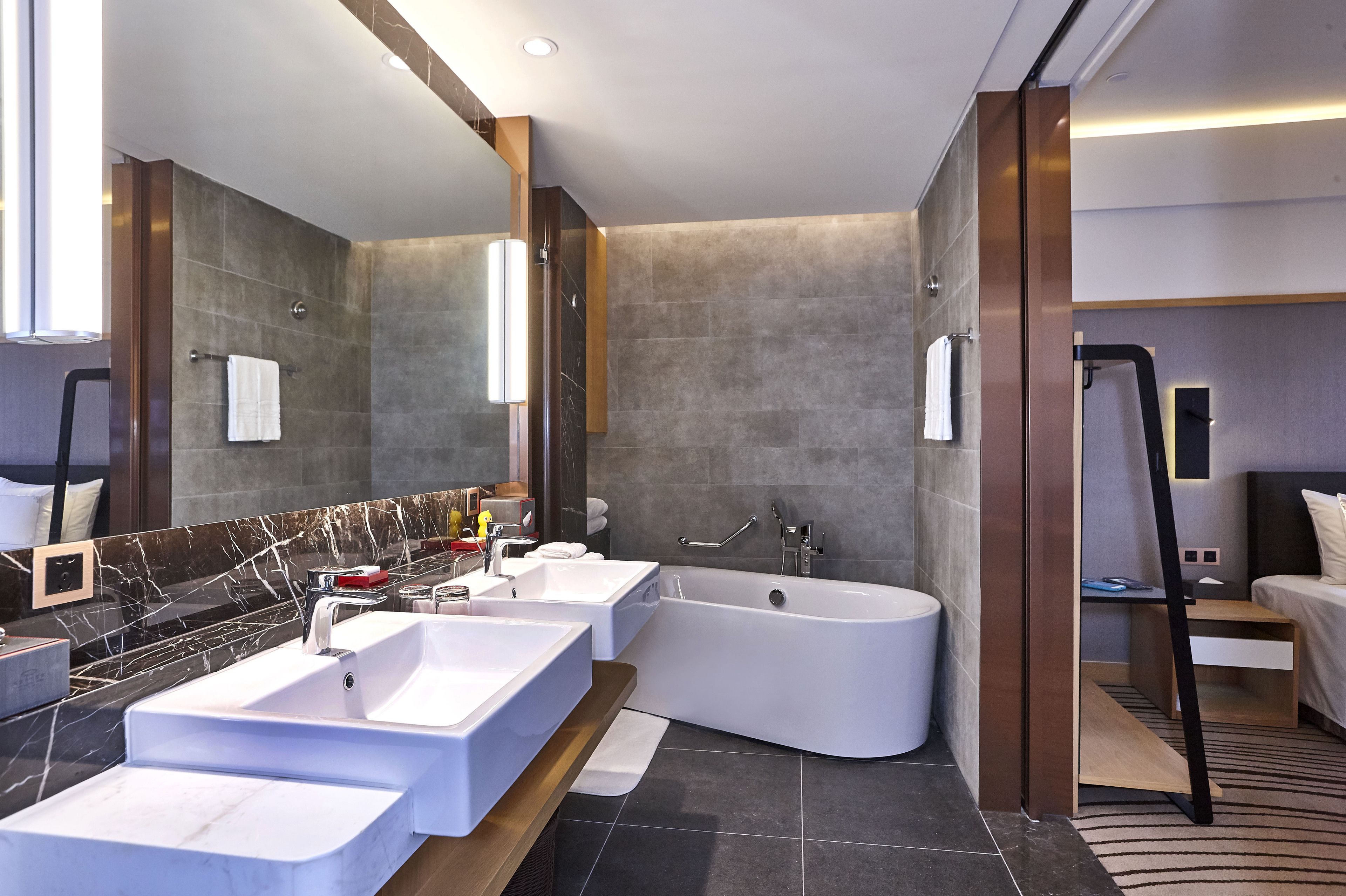 A modern bathroom with a large bathtub, two sinks, and a mirror.