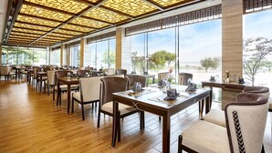 Un restaurante espacioso con suelo de madera, techos altos con diseños intrincados y grandes ventanales que ofrecen vistas al exterior.
