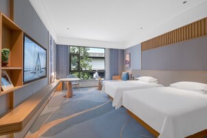 A modern hotel room with two beds, a TV, a desk, and a view of the outdoors.