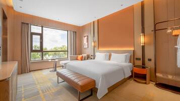 Habitación de hotel moderna con una cama grande, un banco, un escritorio y vistas al exterior.