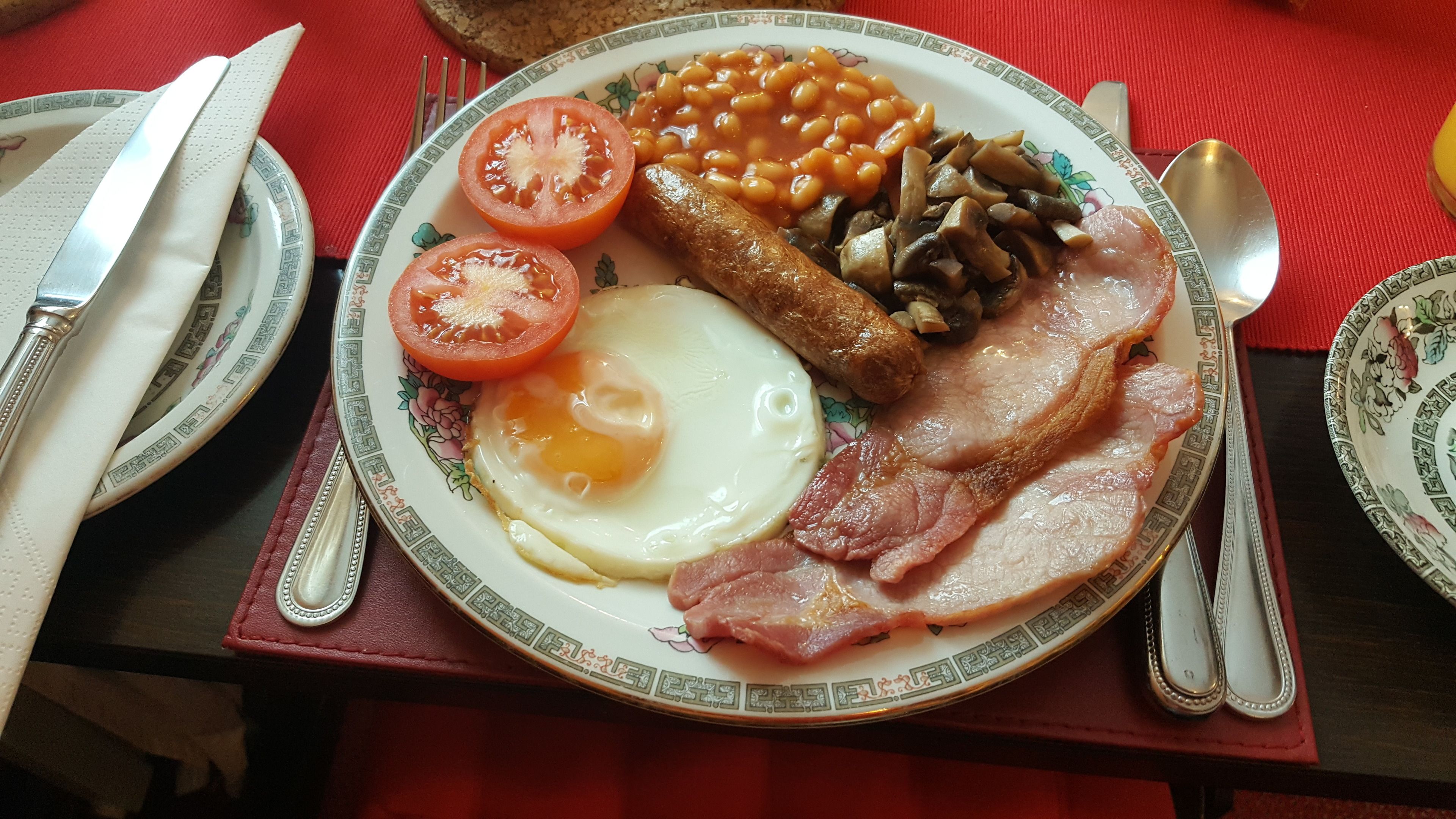 A plate of breakfast food including eggs, bacon, sausages, beans, and tomatoes.
