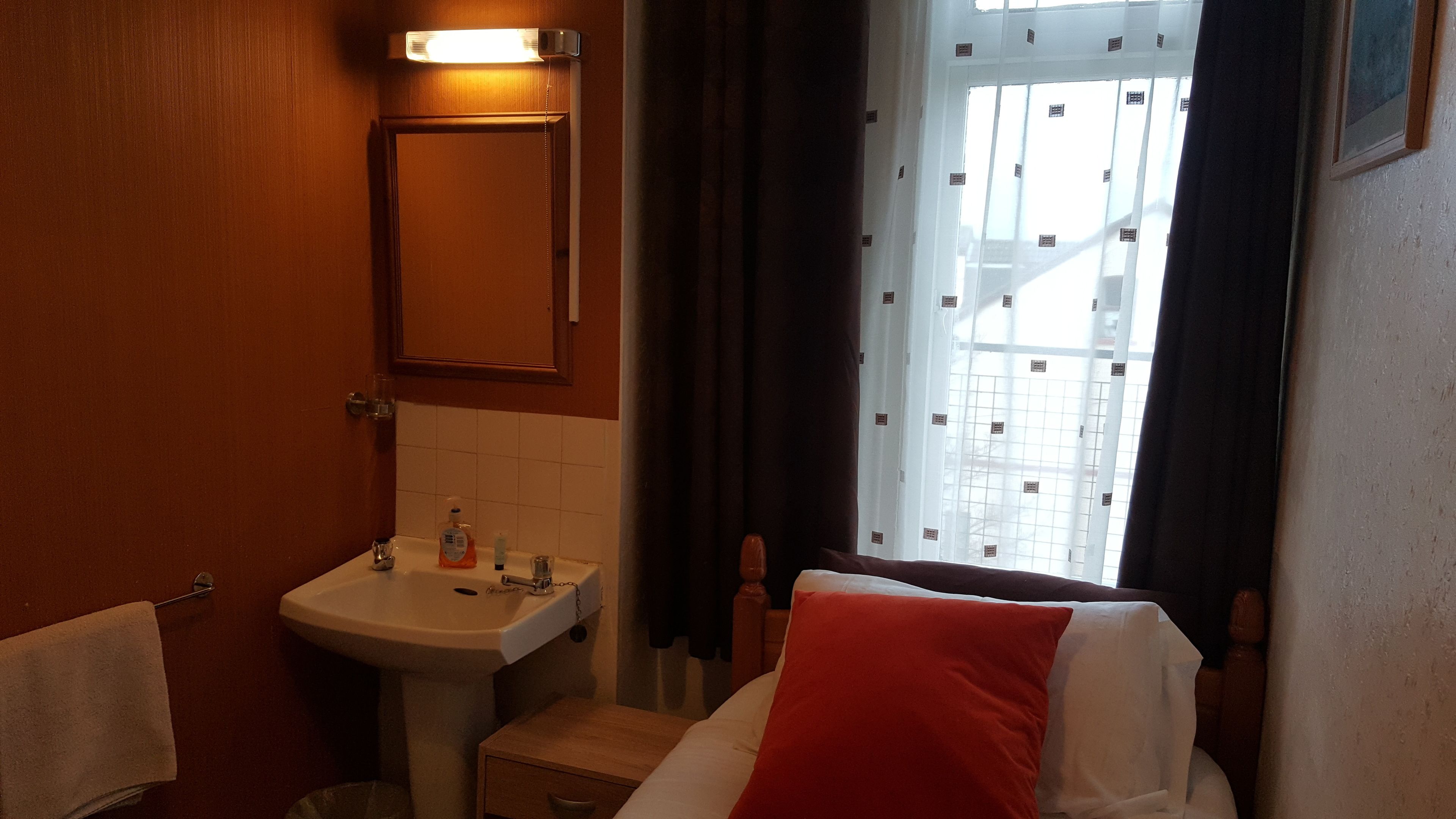 Un baño con lavamanos, espejo y ventana con cortinas.
