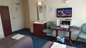 A hotel room with a bed, a desk with a computer, a TV, a mirror, a sink, and a cabinet.