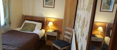 A hotel room with a bed, bedside tables with lamps, a chair, and two framed pictures on the wall.