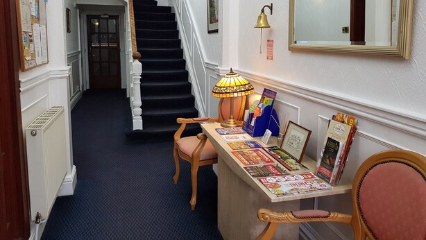 A hallway with a staircase, a desk with magazines, a lamp, and a mirror.