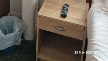 A hotel room with a wooden cabinet above a white sink, a bedside table with a remote control, and a bed with white bedding.