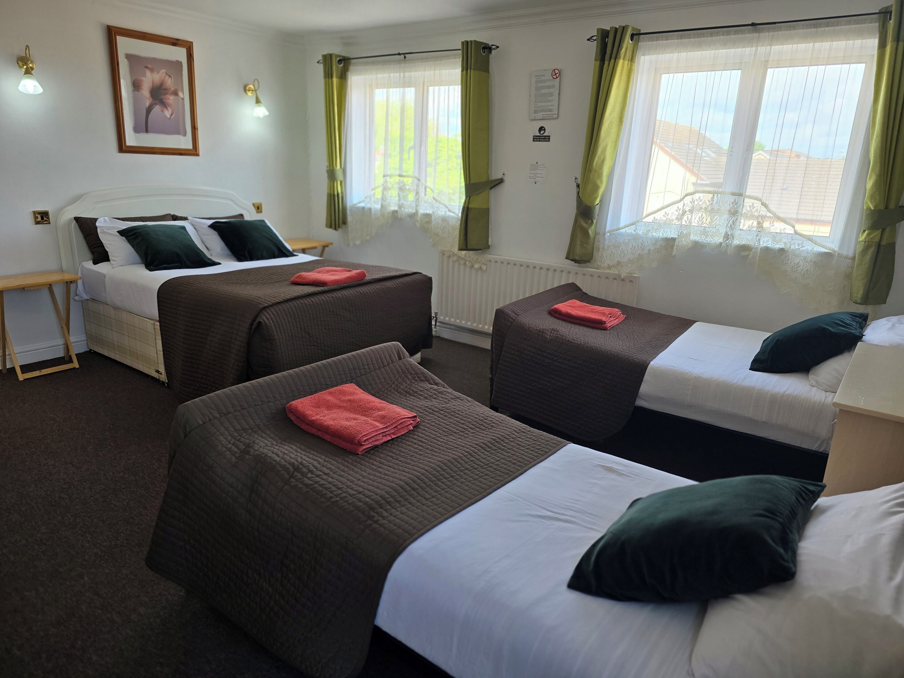 Quarto de hotel com duas camas de solteiro, mesa de cabeceira de madeira, quadro na parede e janela com cortinas.