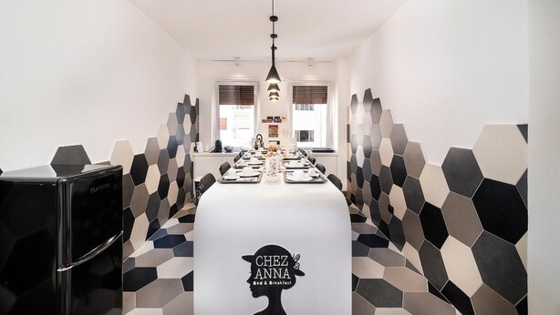 A modern dining area with a long table set for breakfast, a black refrigerator, and hexagonal patterned walls. - Chez Anna B&B (Naples)