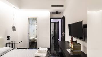 Habitación de hotel moderna con cama, televisor, escritorio y baño visible a través de una puerta abierta.