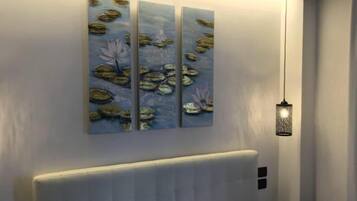 Une chambre moderne avec un grand lit, une tête de lit et une œuvre d’art représentant des nénuphars, accrochée au mur.