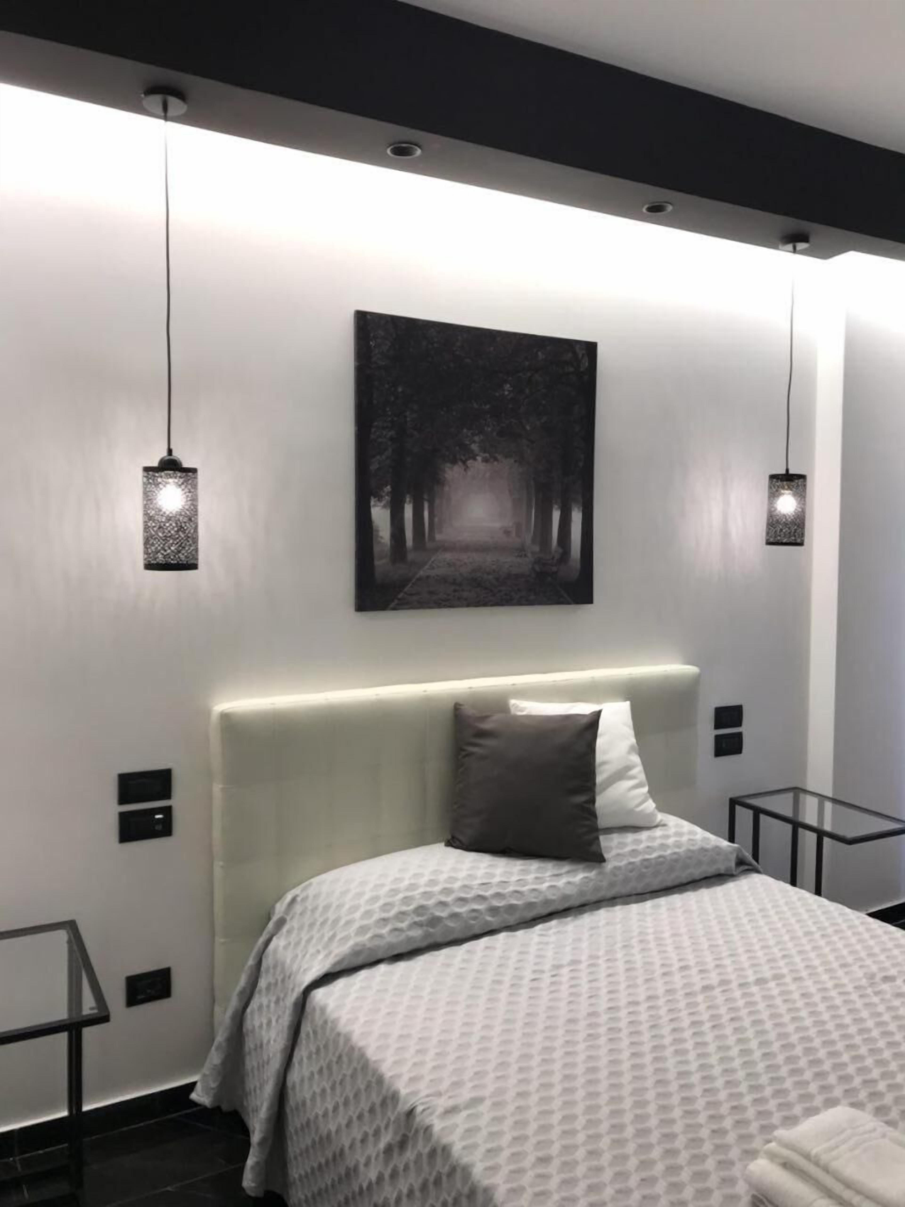 Une chambre moderne avec un grand lit, une tête de lit, une œuvre d’art accrochée au mur et des lampes suspendues.