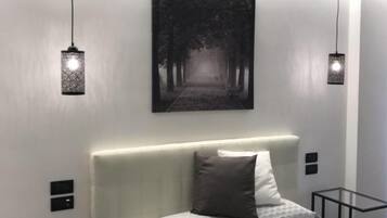 Une chambre moderne avec un grand lit, une tête de lit, une œuvre d’art accrochée au mur et des lampes suspendues.