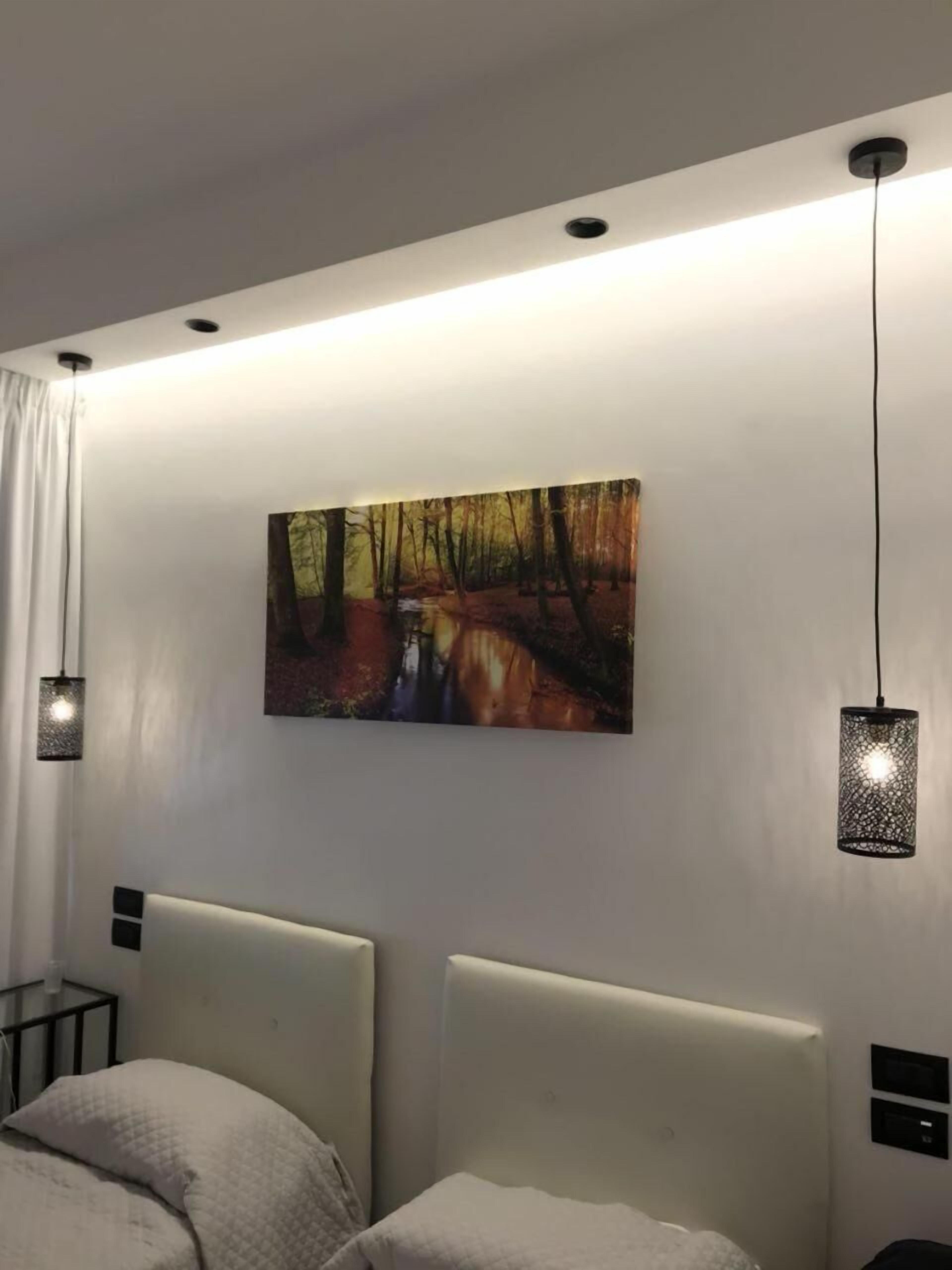 Een moderne slaapkamer met een groot bed, een schilderij van een bospad, en hanglampen.