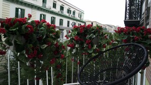 A balcony with red flowers and a black wicker chair. - Chez Anna B&B (Naples)