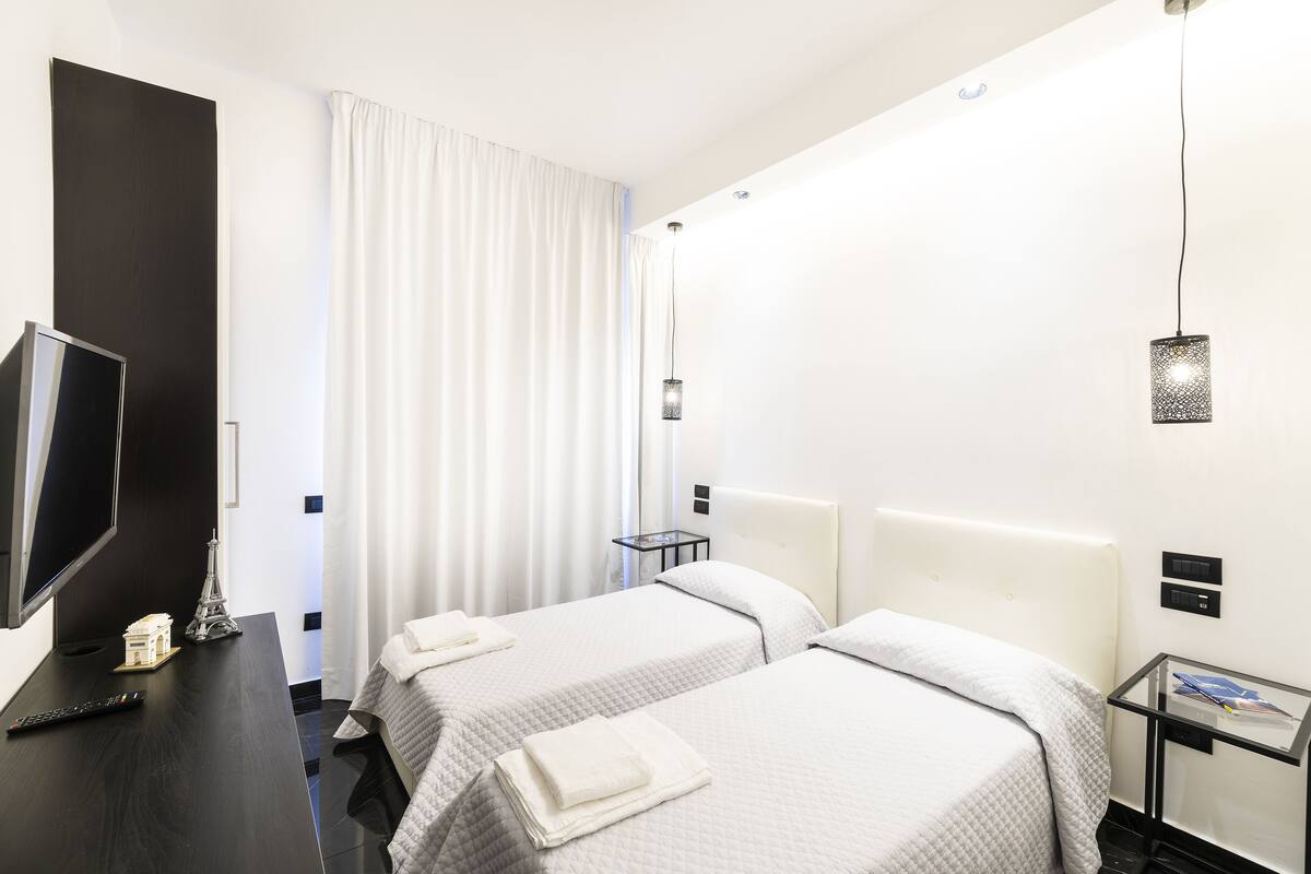 Une chambre d’hôtel avec deux lits, un bureau avec une télévision et une petite table avec une lampe.