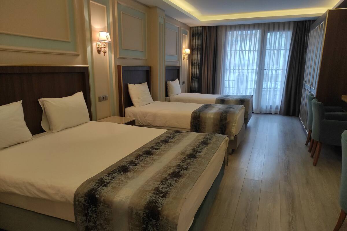 Habitación de hotel con tres camas, piso de madera y vistas al exterior a través de amplios ventanales.