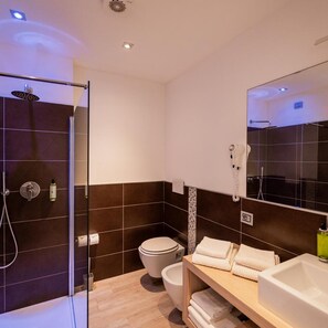 A modern bathroom with a glass-enclosed shower, a toilet, and a vanity with a sink and towel rack. - Hotel Piccadilly (Jesolo)