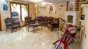 A spacious living room with a fireplace, a vintage motorcycle, and a large window. - Foca Ensar Hotel (Foça)