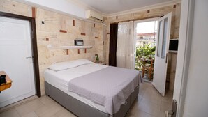 A bedroom with a bed, a shelf with a radio, a door, and a view of the outside. - Foca Ensar Hotel (Foça)