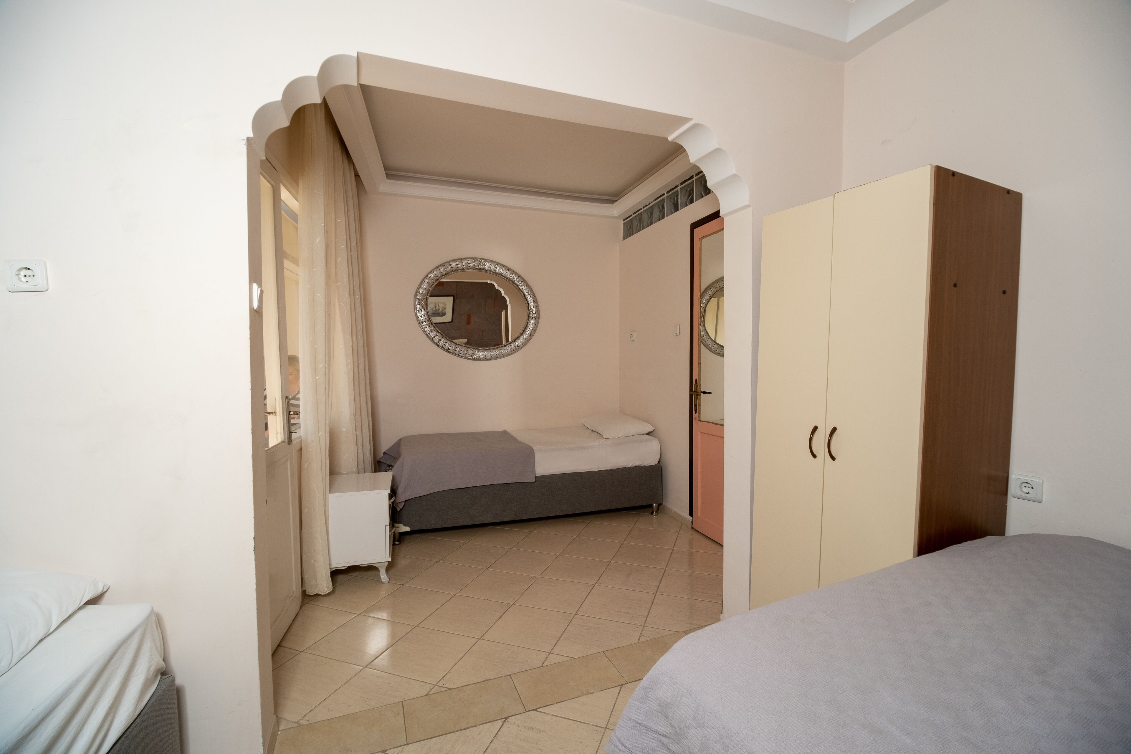 Een slaapkamer met een bed, een kledingkast, een spiegel en een deur naar een andere kamer.