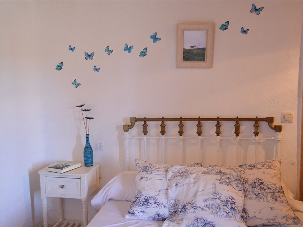 A bedroom with a bed, a nightstand, a vase, and butterfly decals on the wall.