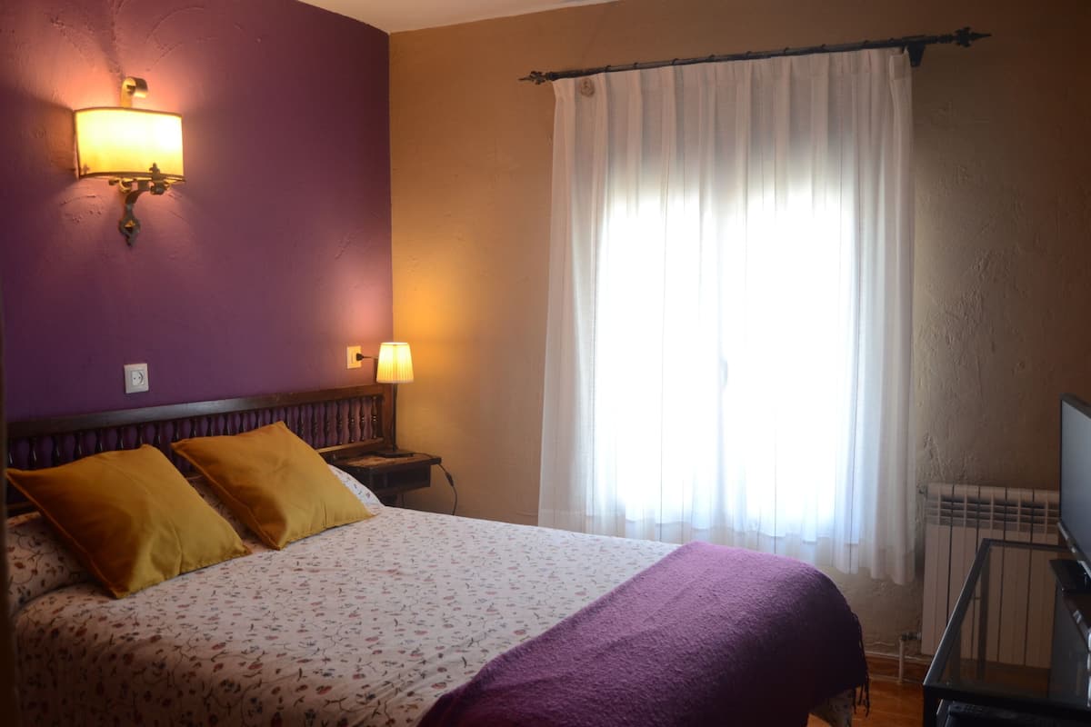 Een hotelkamer met een bed, twee wandlampen, een raam met gordijnen en een radiator.