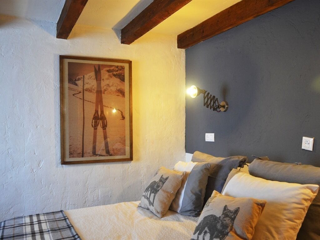 Un dormitorio con una cama, almohadas, un cuadro enmarcado y una lámpara fijada a la pared.