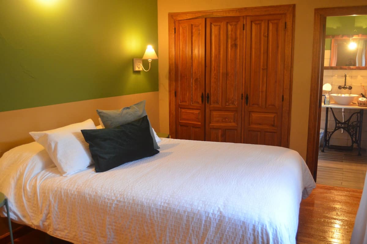 Een slaapkamer met een bed, een groene wand, een houten garderobe en een badkamer zichtbaar door een open deur.