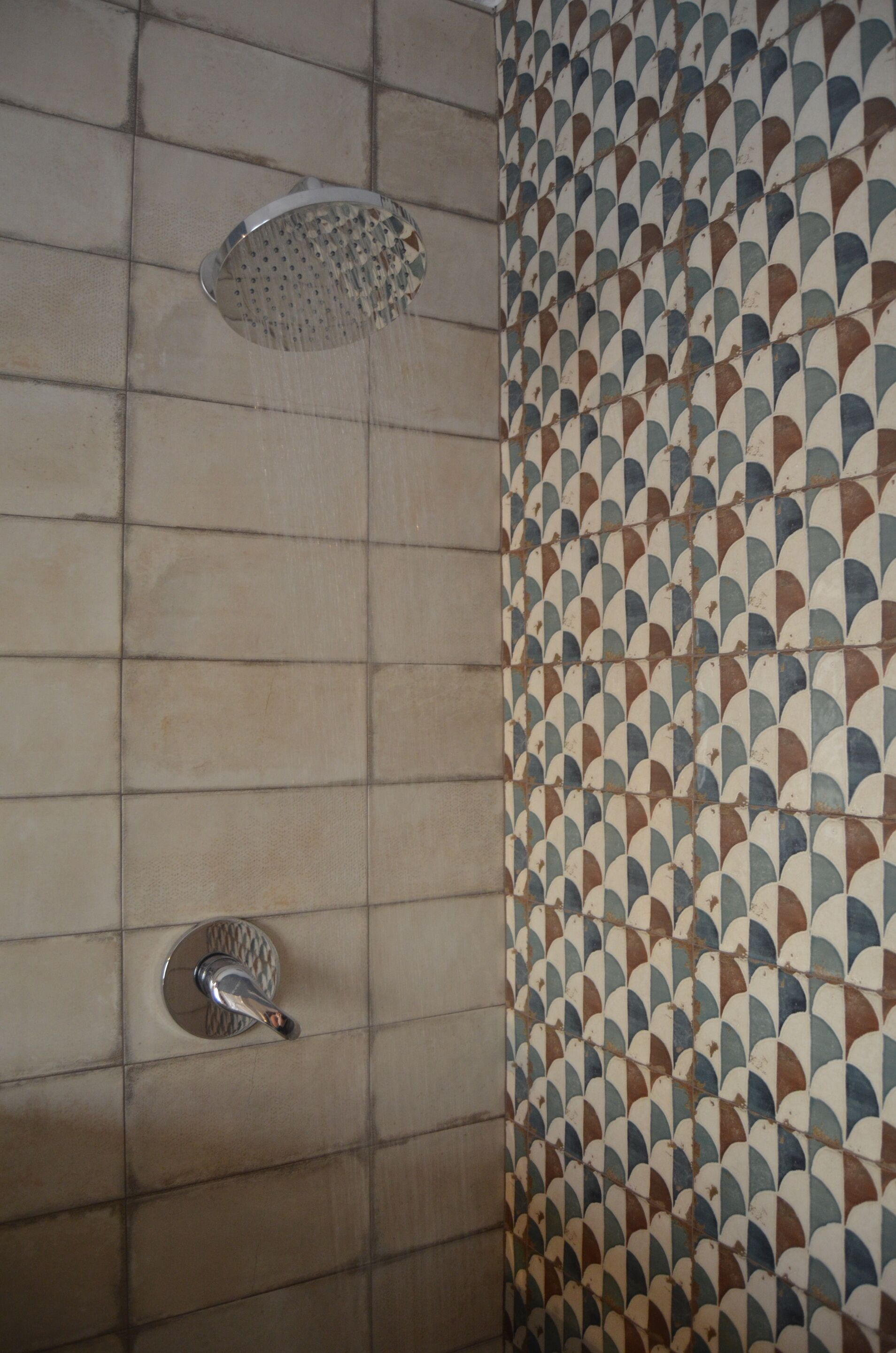 A shower with a rain showerhead and a handheld showerhead, tiled walls with a geometric pattern, and a visible shower control panel.