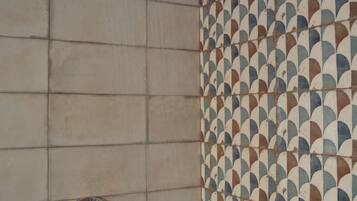 A shower with a rain showerhead and a handheld showerhead, tiled walls with a geometric pattern, and a visible shower control panel.