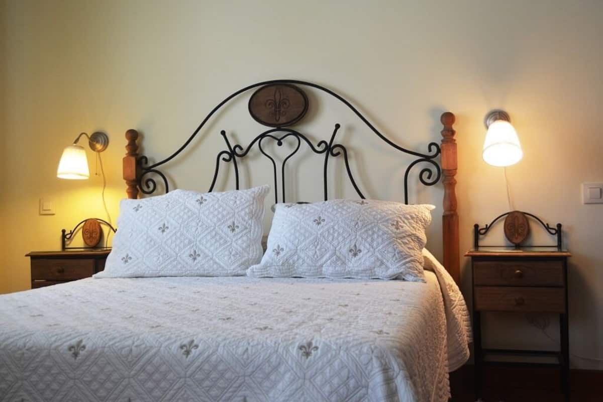 Een net opgemaakt bed met een gewatteerde witte spreideken en twee passende kussens, omringd door twee nachtkastjes met lampen.