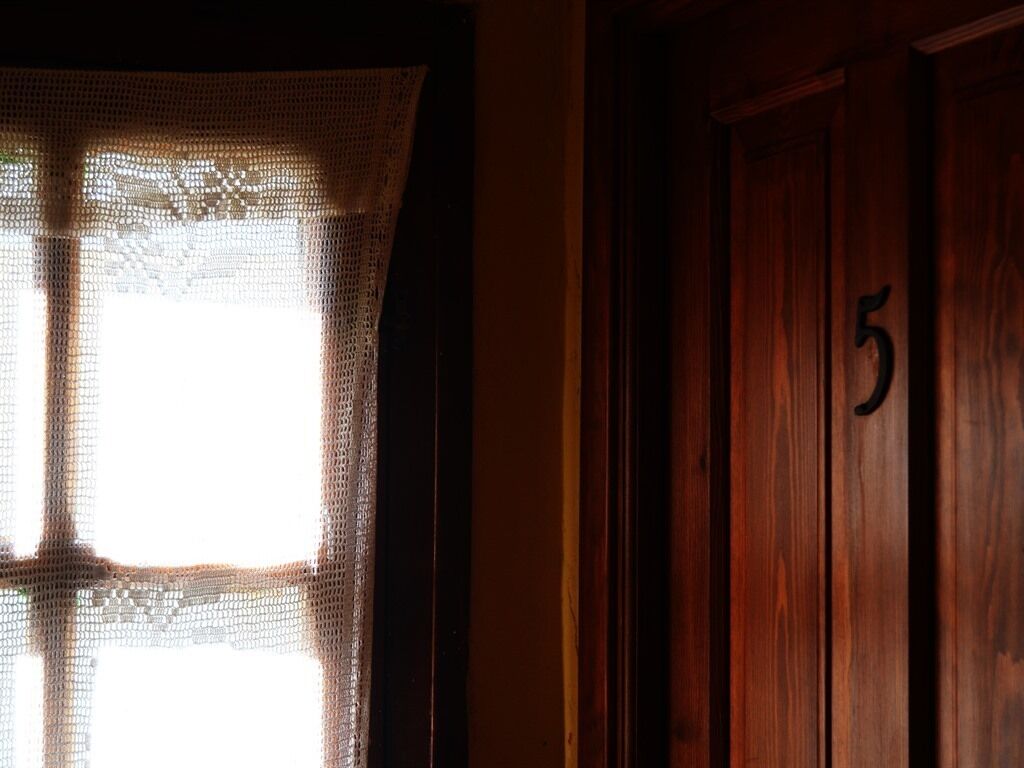 A wooden door with the number 5, a window with a lace curtain, and a dark interior.