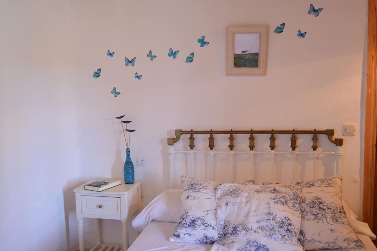 Een slaapkamer met een bed, een nachtkastje, een vaas en vlinderstickers op de muur.