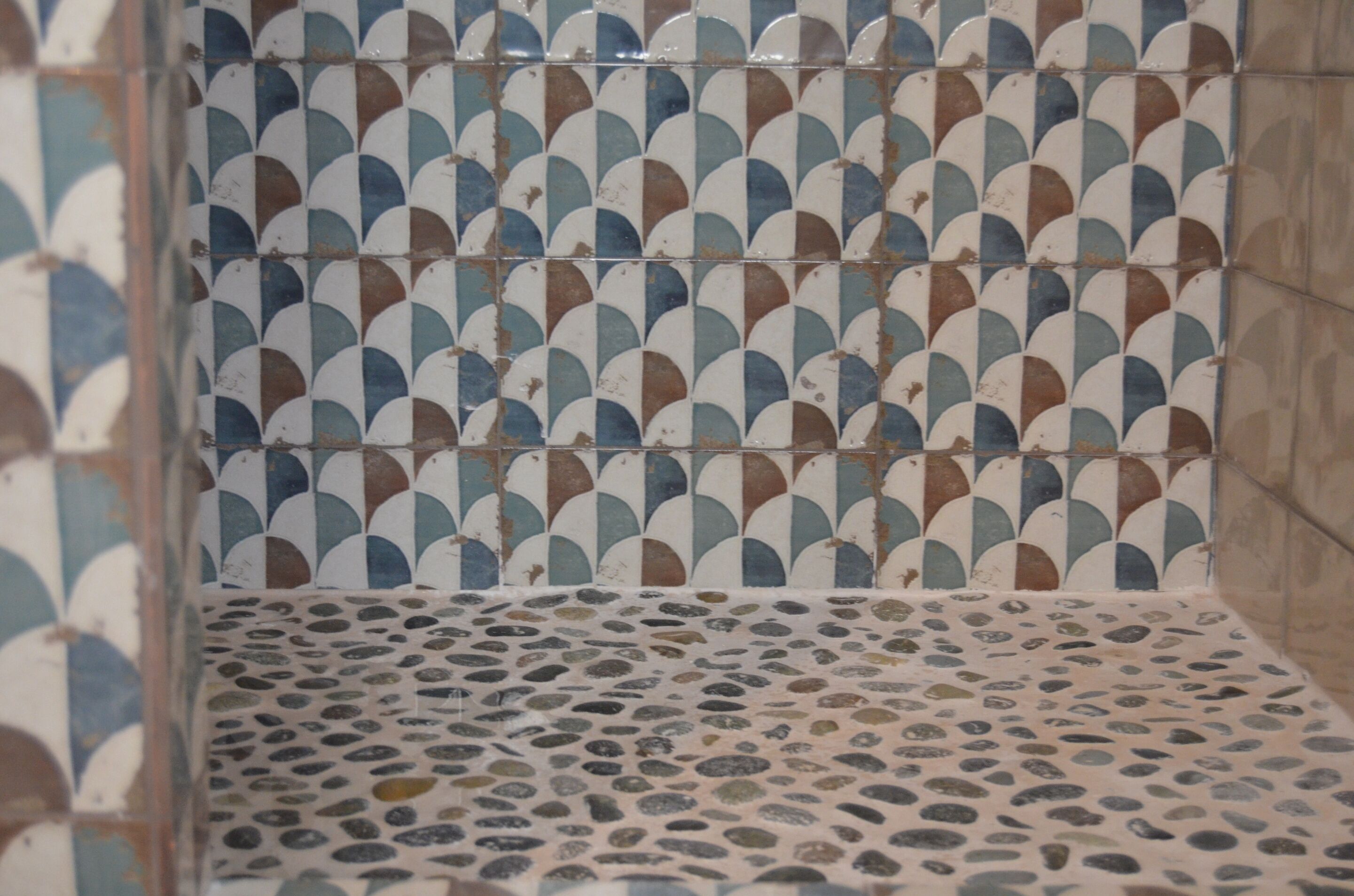 A tiled shower area with a geometric pattern and pebble-like floor design.