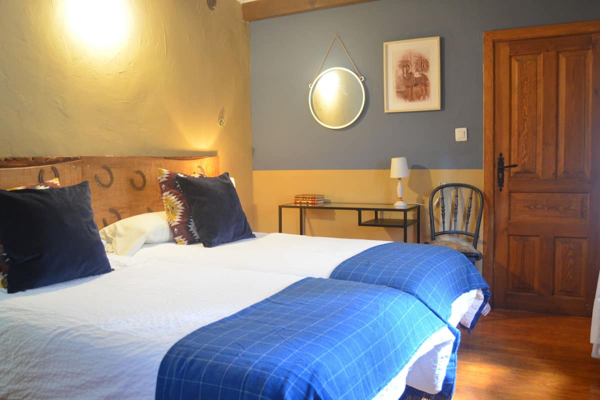 Een slaapkamer met een bed, nachtkastje, stoel, deur en een spiegel aan de muur.