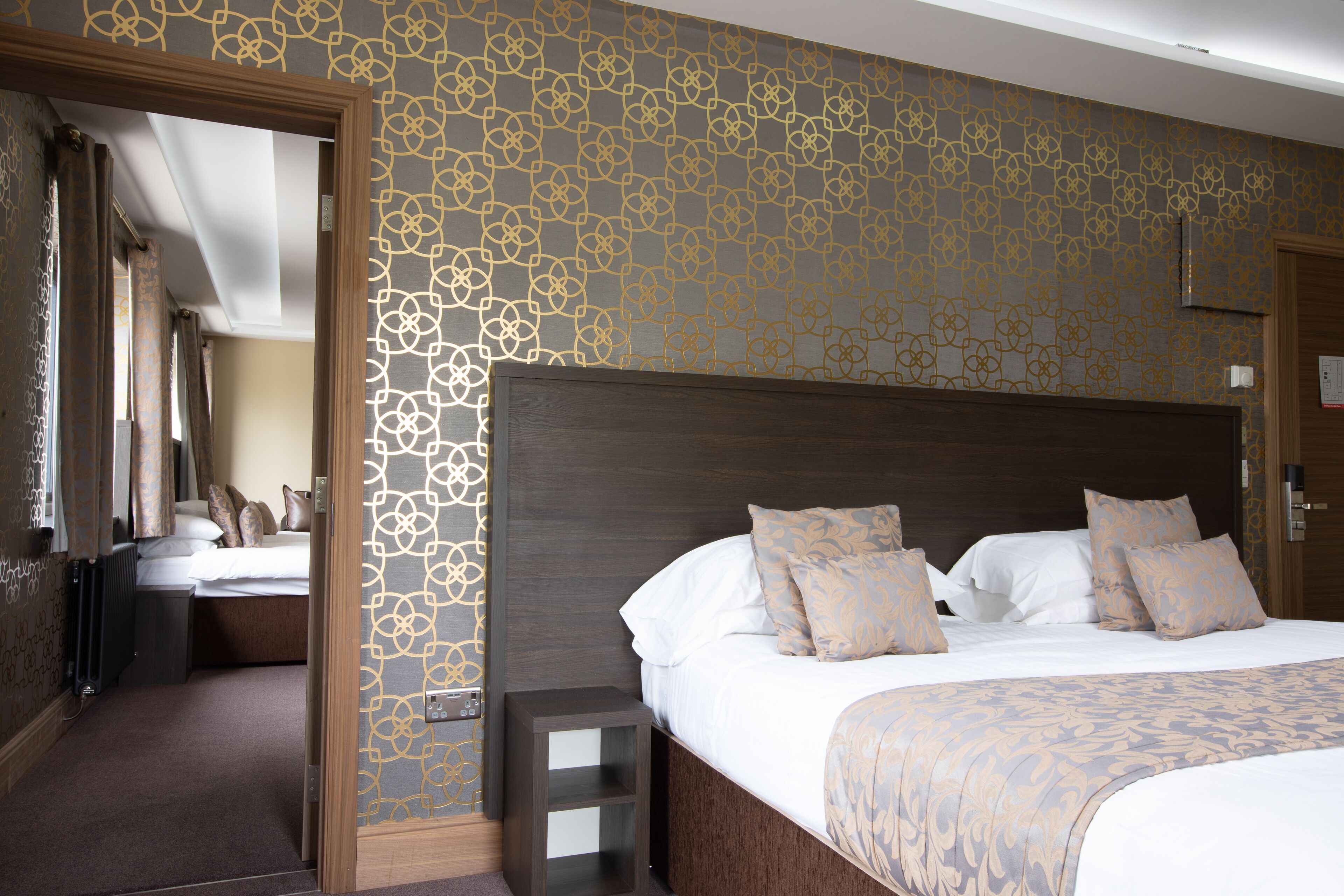 A hotel room with a large bed, a wooden headboard, and a patterned wall.