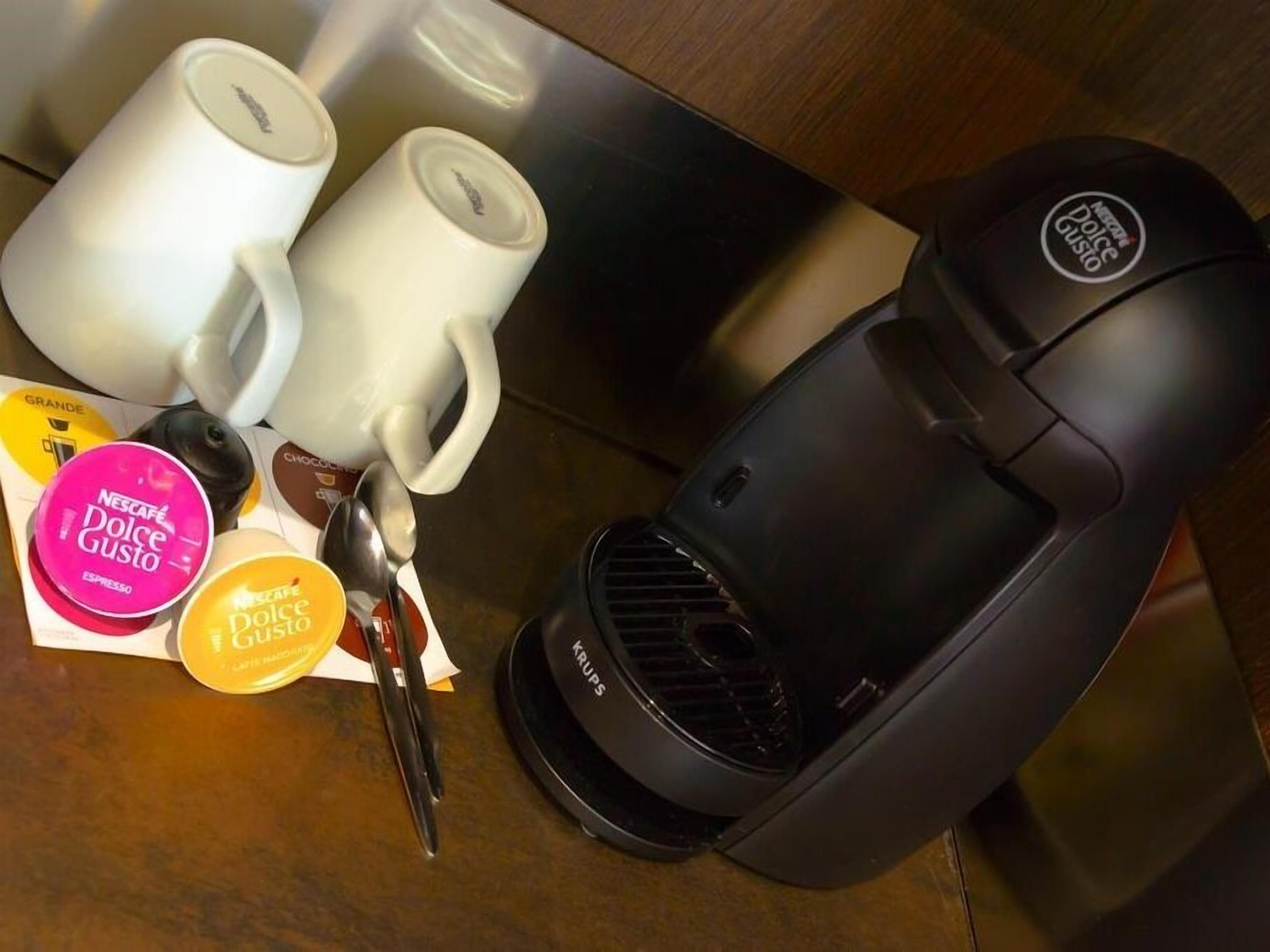 Eine Kaffeemaschine, zwei weiße Tassen und ein Schlüsselsatz auf einer Holztischplatte.
