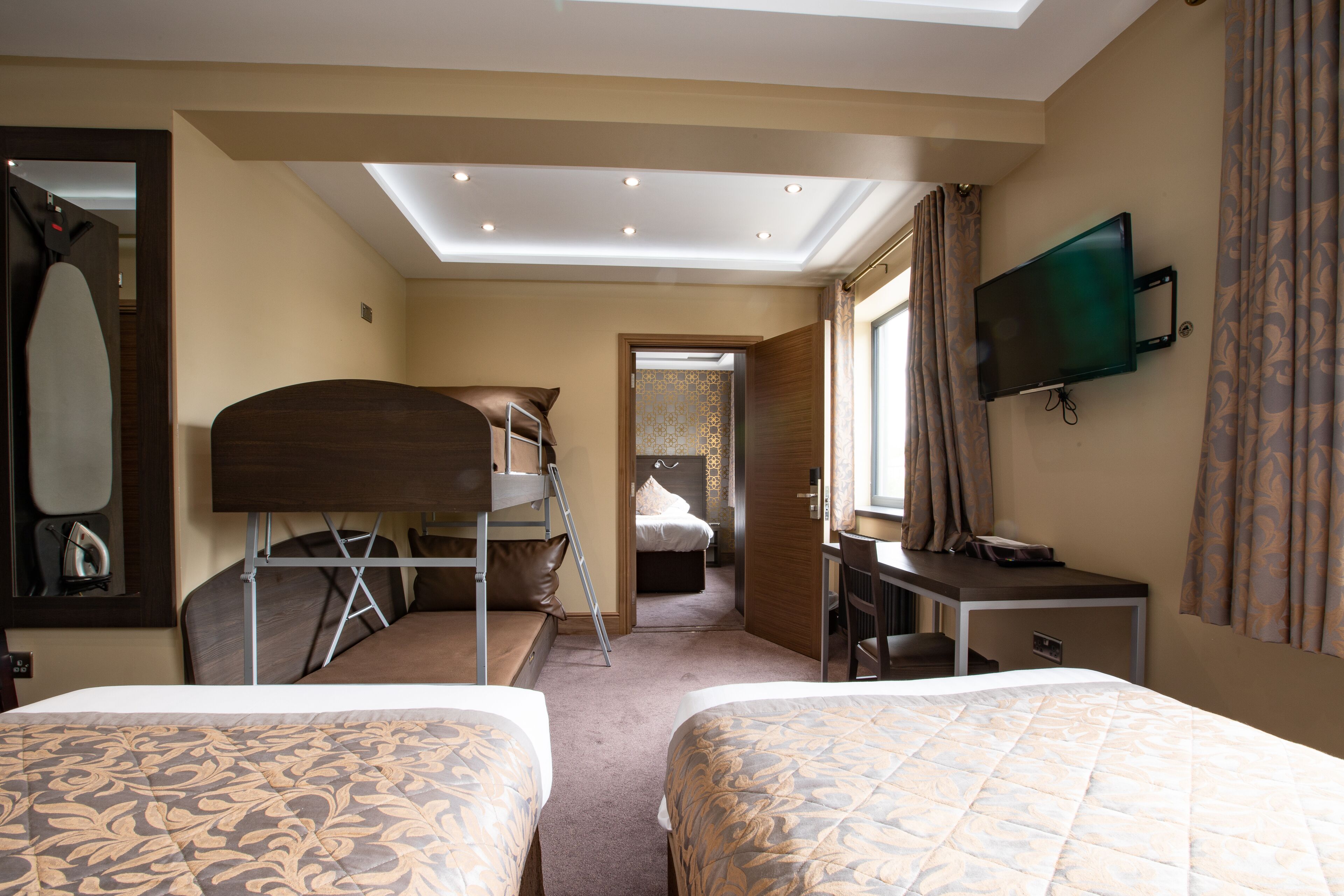 A hotel room with two beds, a desk, a television, and a skylight.