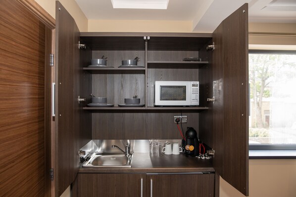 A compact kitchen with a microwave, coffee maker, and a sink.