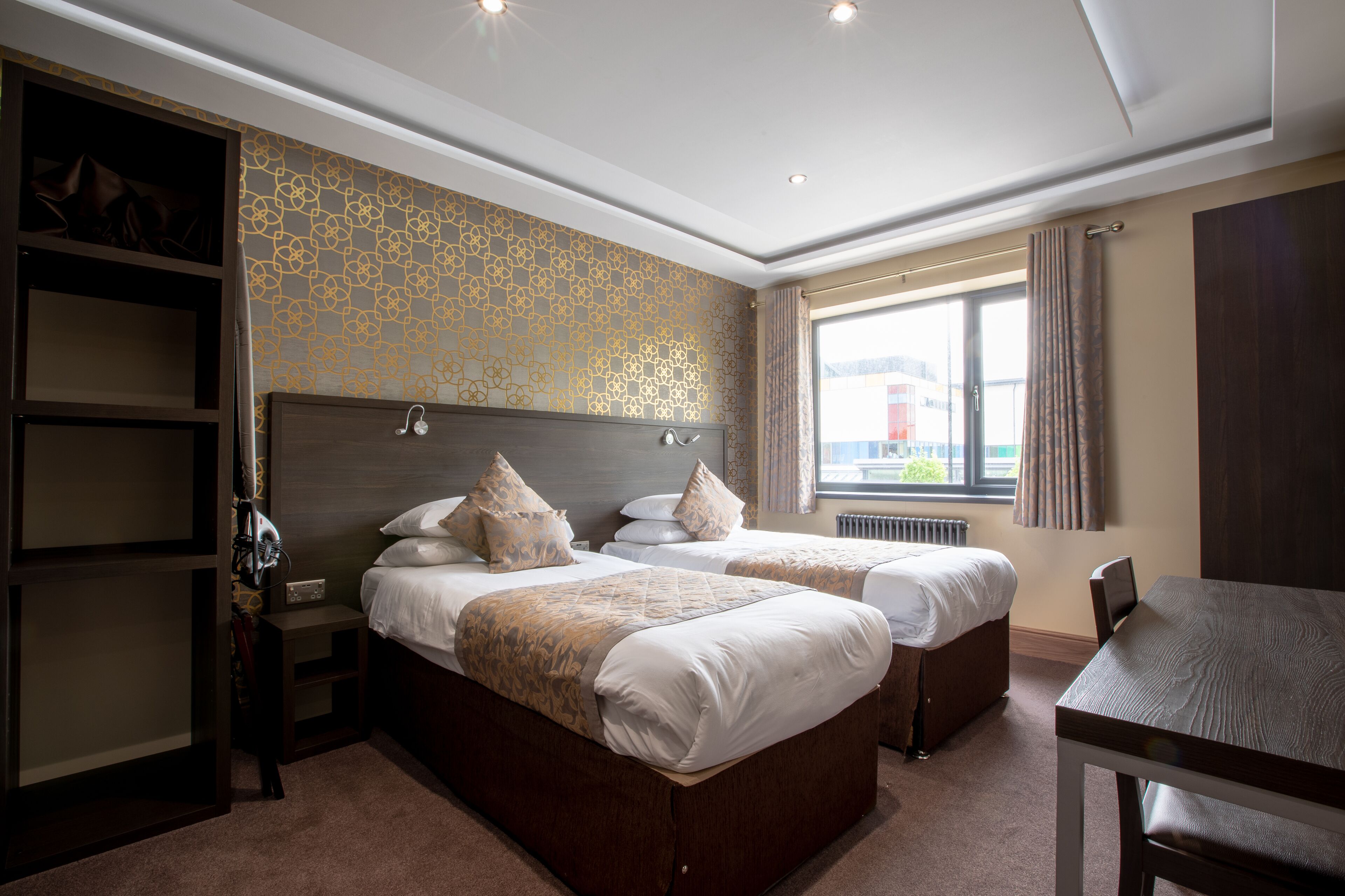 A hotel room with two beds, a desk, and a wardrobe.
