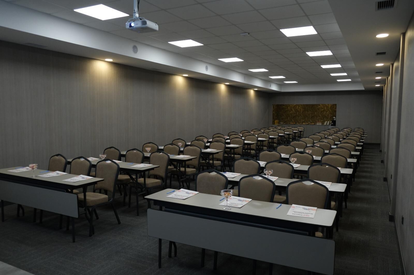 A conference room with rows of tables and chairs, equipped with projectors and overhead lighting.