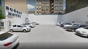 Een parkeerplaats met meerdere auto's voor een gebouw met de tekst 'BUCDAY HOTEL' en 'OTOPARK'.