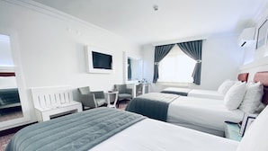 Quarto de hotel com duas camas, uma escrivaninha, uma cadeira, uma televisão e uma janela com cortinas.