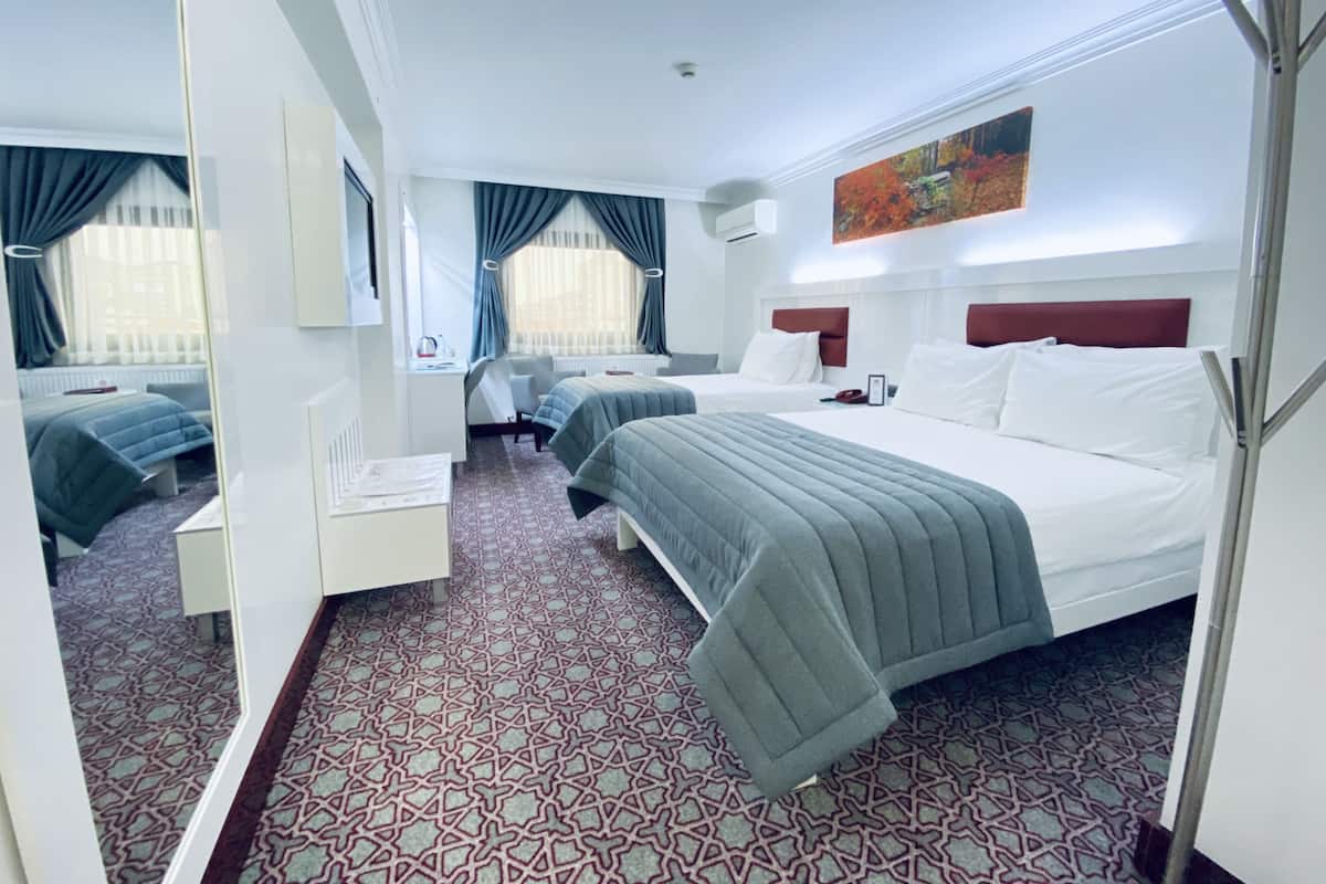 A hotel room with two beds, a desk, and a chair. There is a window with curtains, a painting on the wall, and a patterned carpet.