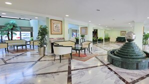 Um hall amplo com piso de mármore, áreas de estar e uma fonte decorativa central.