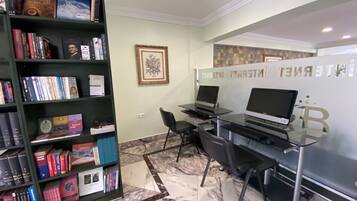 A library with bookshelves, two laptops on desks, a framed picture on the wall, and a marble floor.