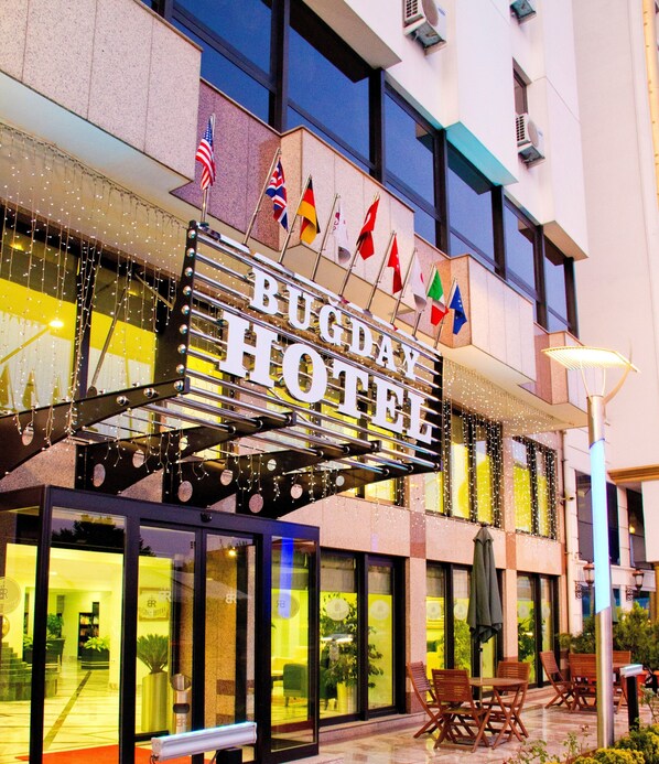 A hotel sign with multiple flags, large windows, and outdoor seating. - Bugday Hotel (Ankara)